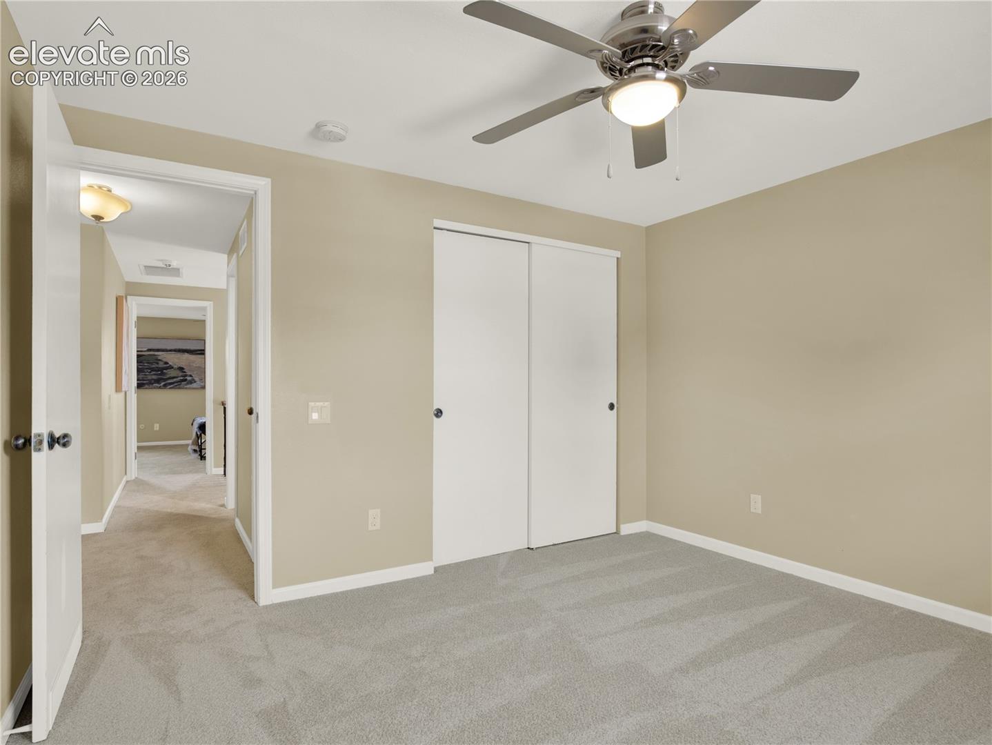 Interior room featuring neutral wall paint, wall-to-wall carpeting, a multi-blade ceiling fan with an integrated light fixture, and a built-in closet with sliding doors
