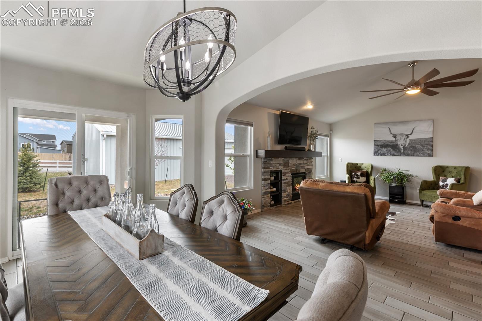 Dining area featuring a contemporary chandelier, opening to a living area with a gas fireplace, integrated shelving, and a ceiling fan