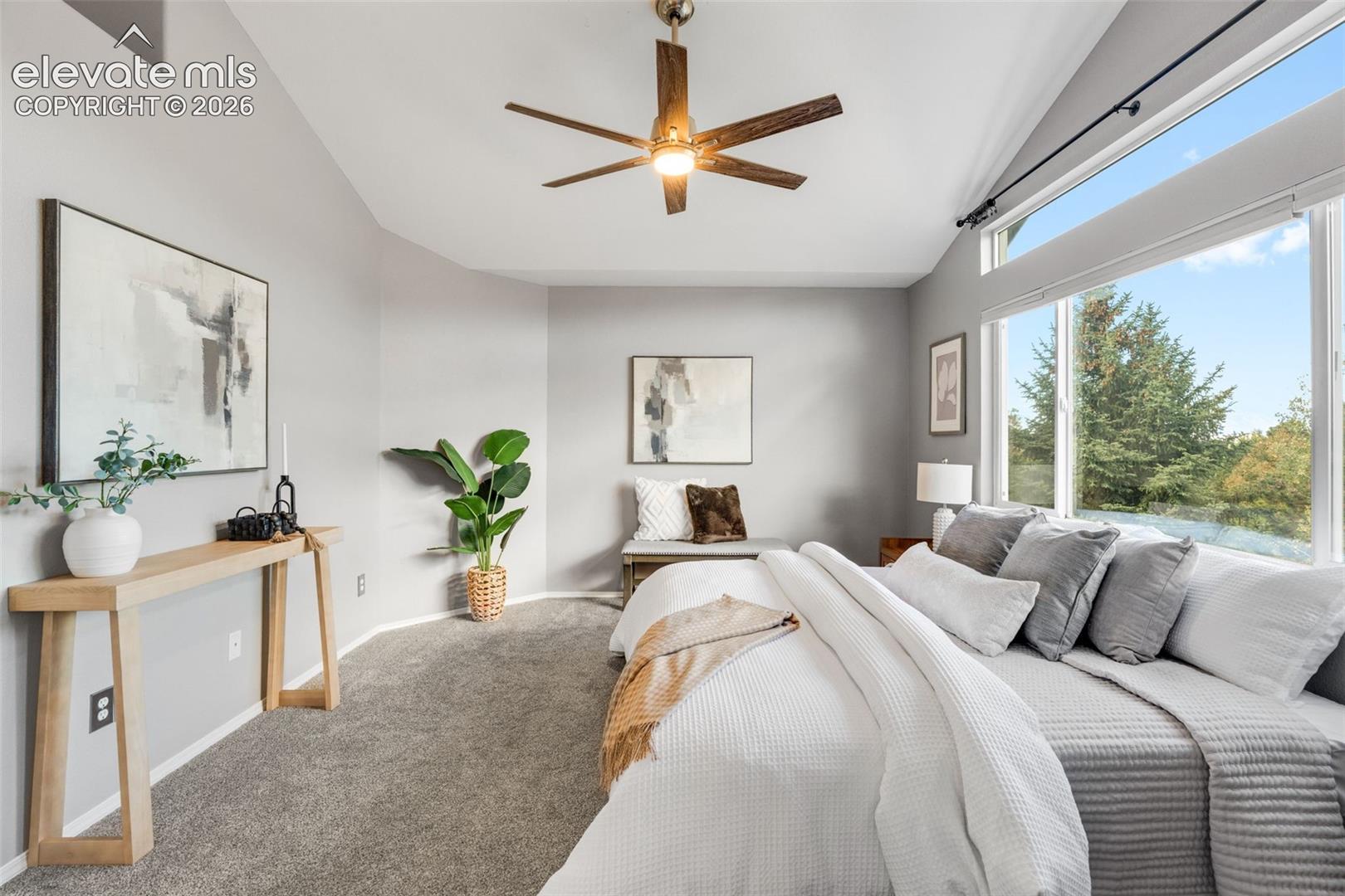 Vaulted ceilings featuring a multi-blade wood-finish ceiling fan with integrated lighting, large windows, and wall-to-wall carpeting