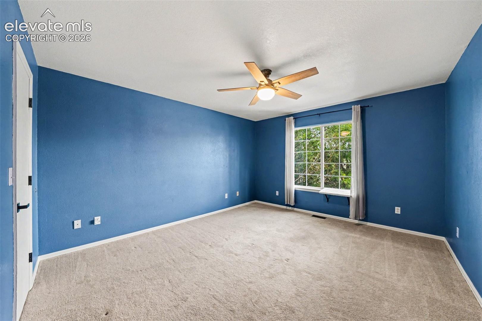 Spacious room with plush carpeting, a large window, and a ceiling fan