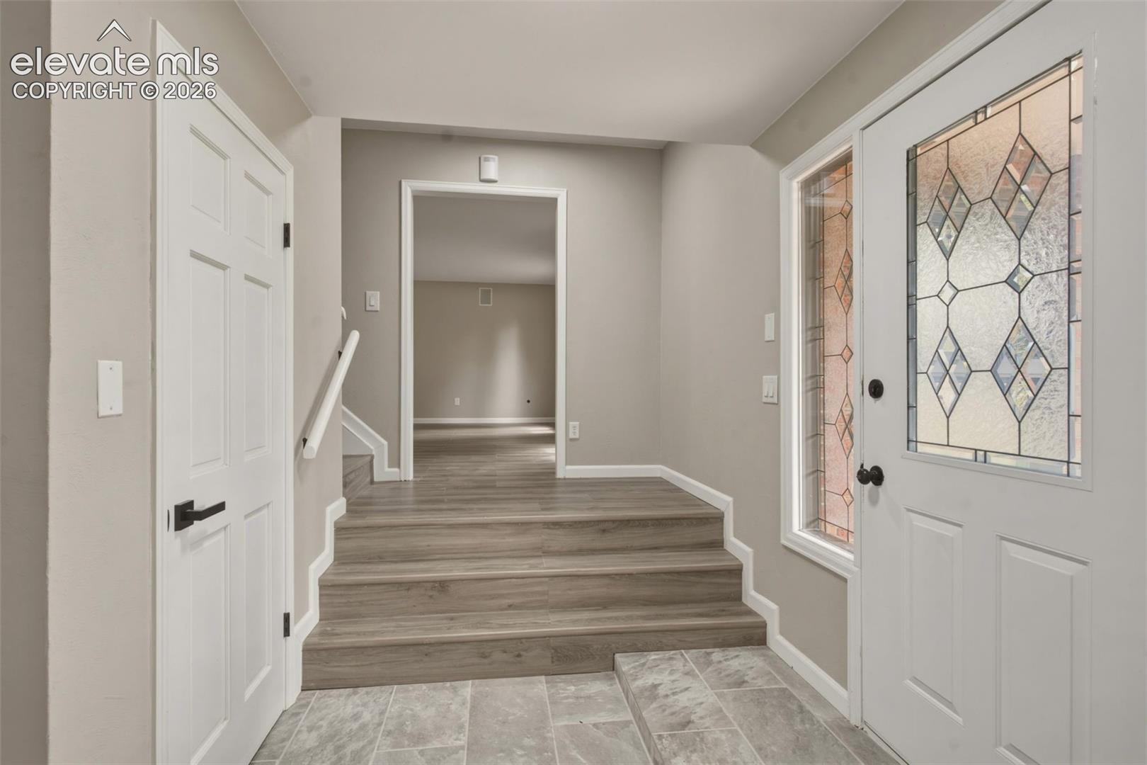 Entryway featuring a white paneled door with decorative glass, tile flooring, and wood-finish stairs