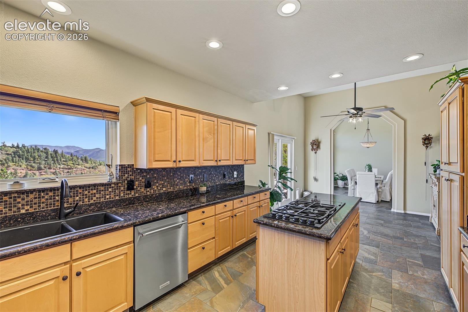Spacious kitchen featuring granite countertops, a center island with gas cooktop, abundant cabinetry, stainless steel dishwasher, tile flooring, and mountain views from the window above the sink.