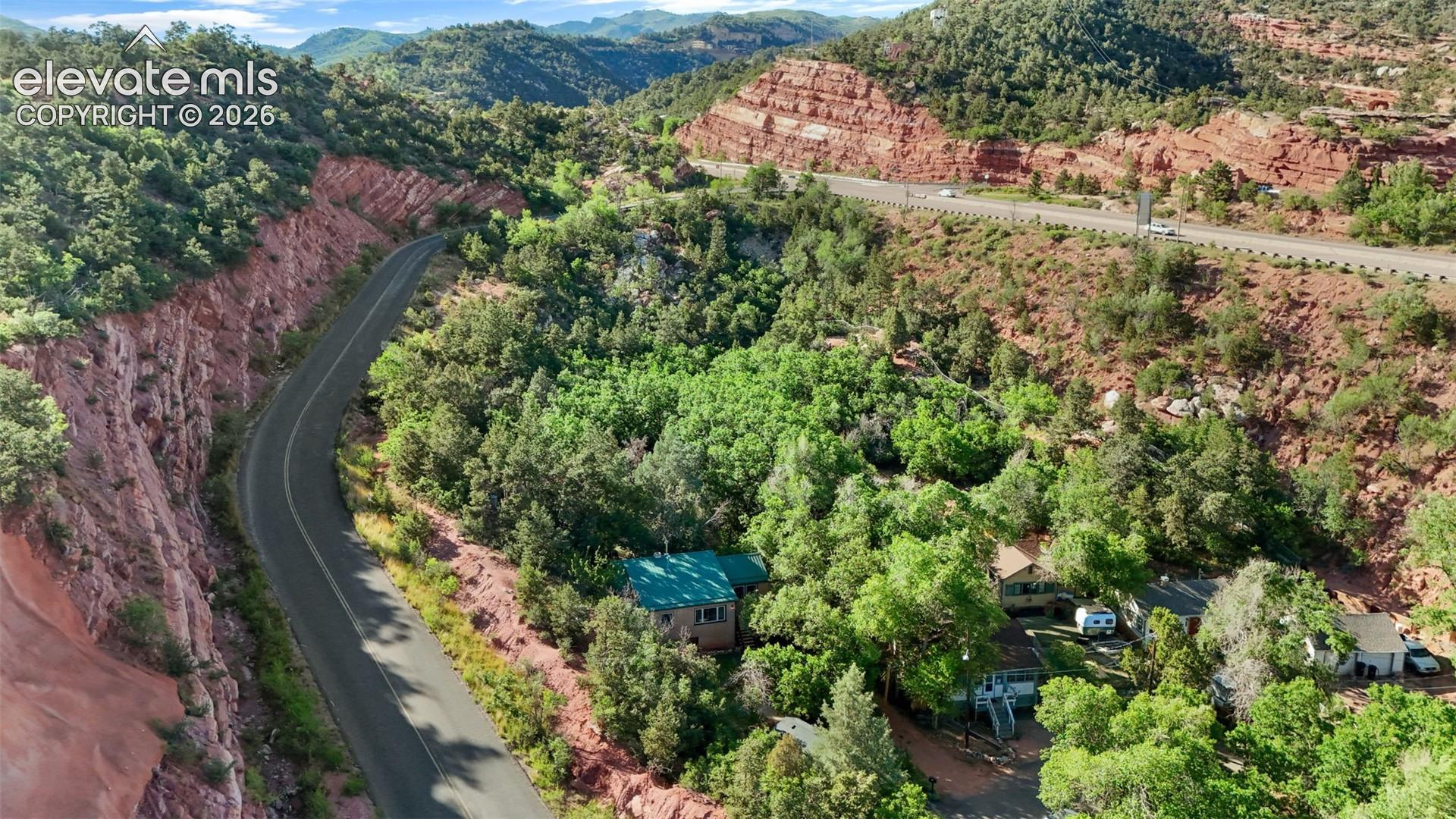 Mountainous landscape featuring verdant trees, red rock formations, and a winding paved road