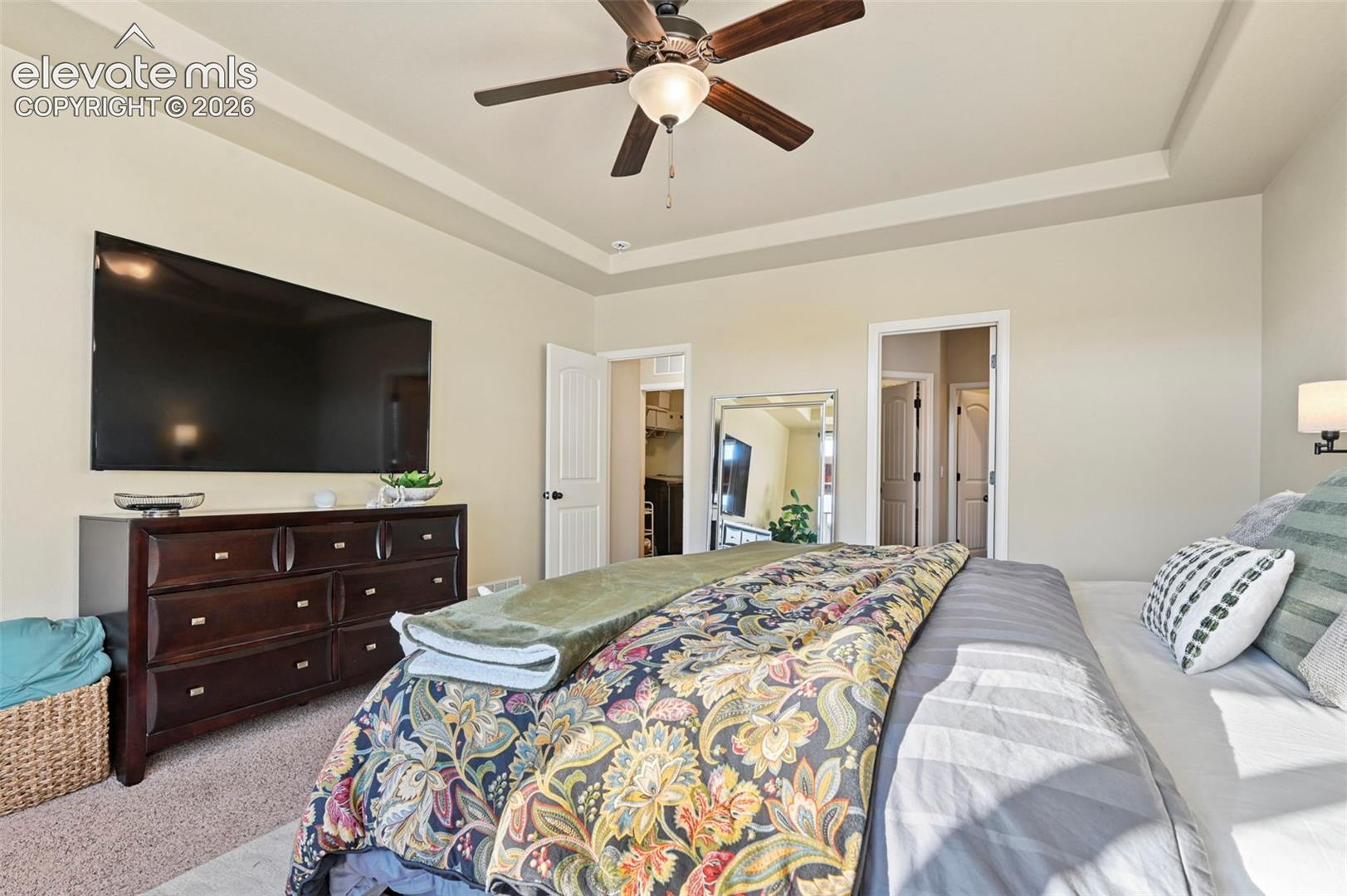 Tray ceiling, ceiling fan with light, wall-mounted television, and sconce lighting