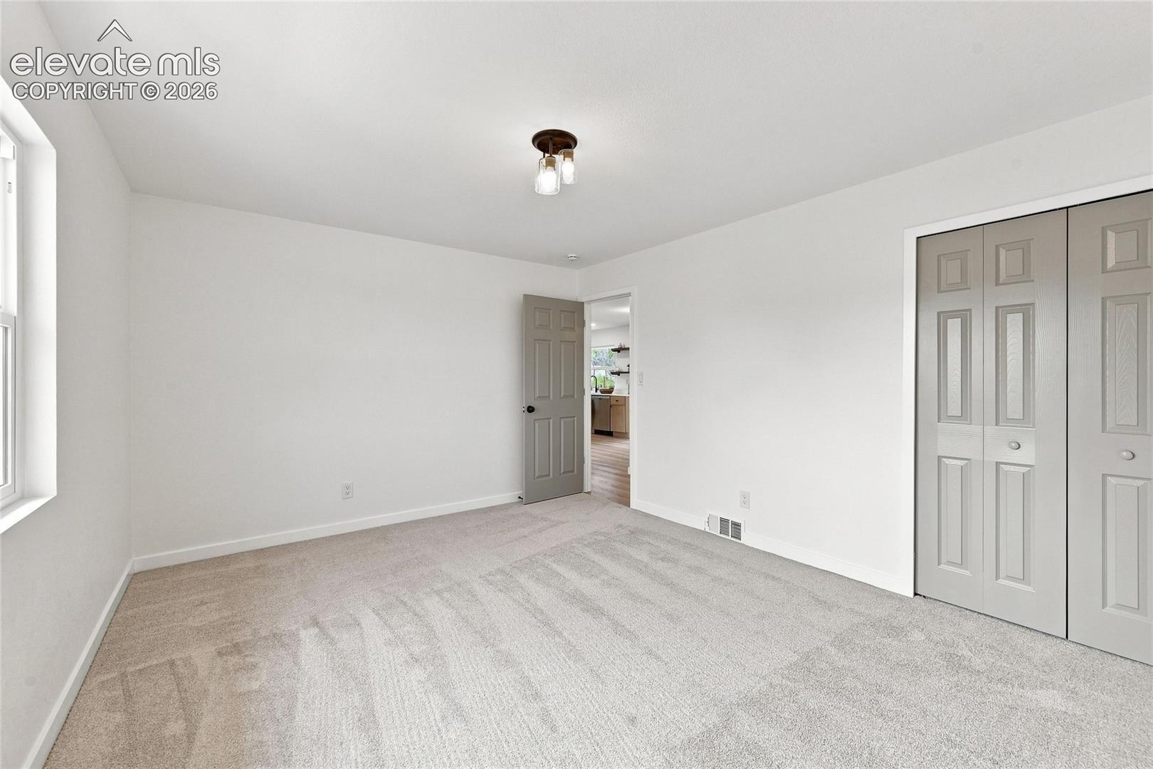 Neutral-toned carpet flooring, white painted walls, natural light window, and a flush-mount ceiling light fixture