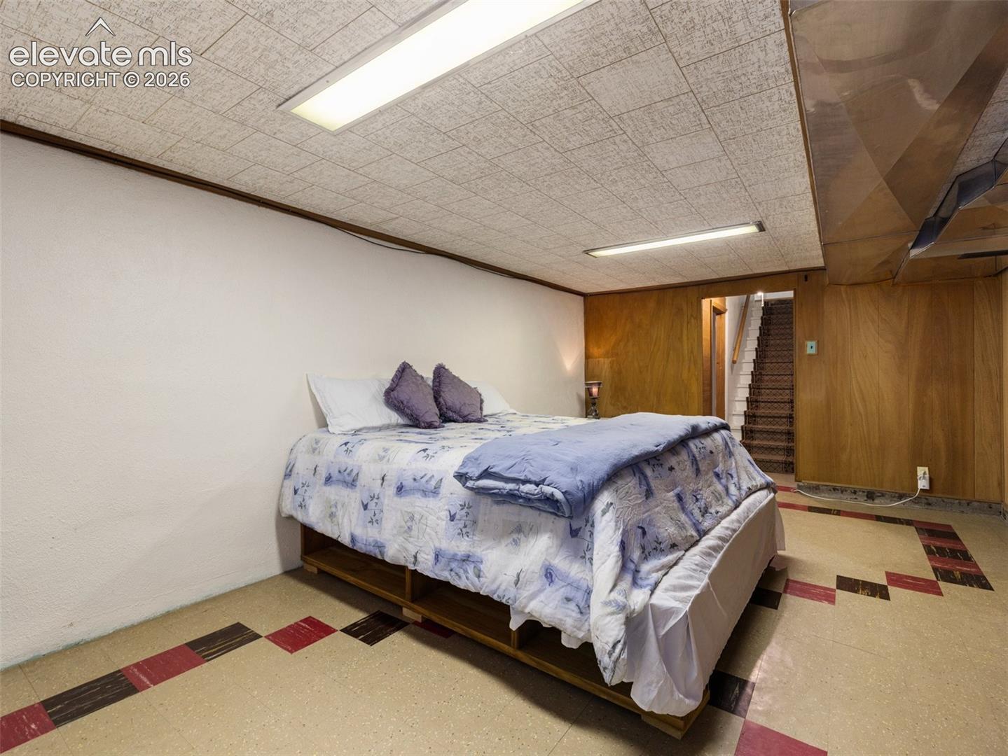 Finished room featuring wood-paneled walls, a suspended ceiling with integrated linear lighting, and patterned tile flooring