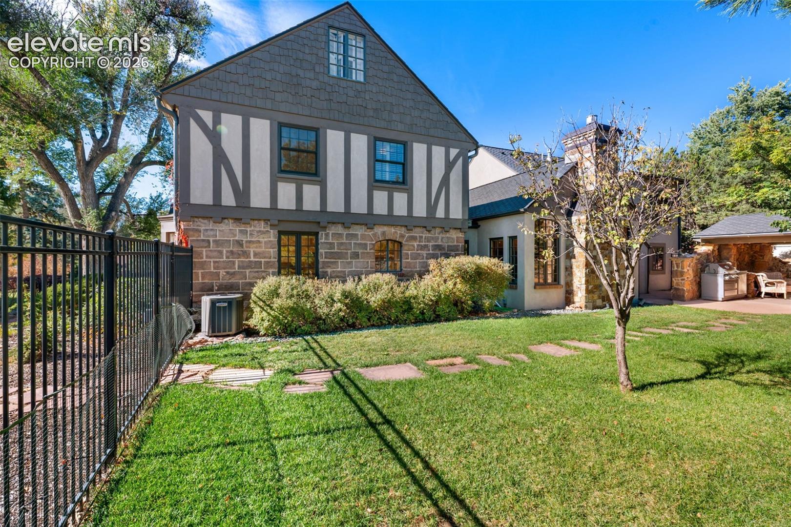 Tudor-style exterior featuring stone masonry, half-timber detailing, shingle siding, a stone chimney, and a covered outdoor kitchen area
