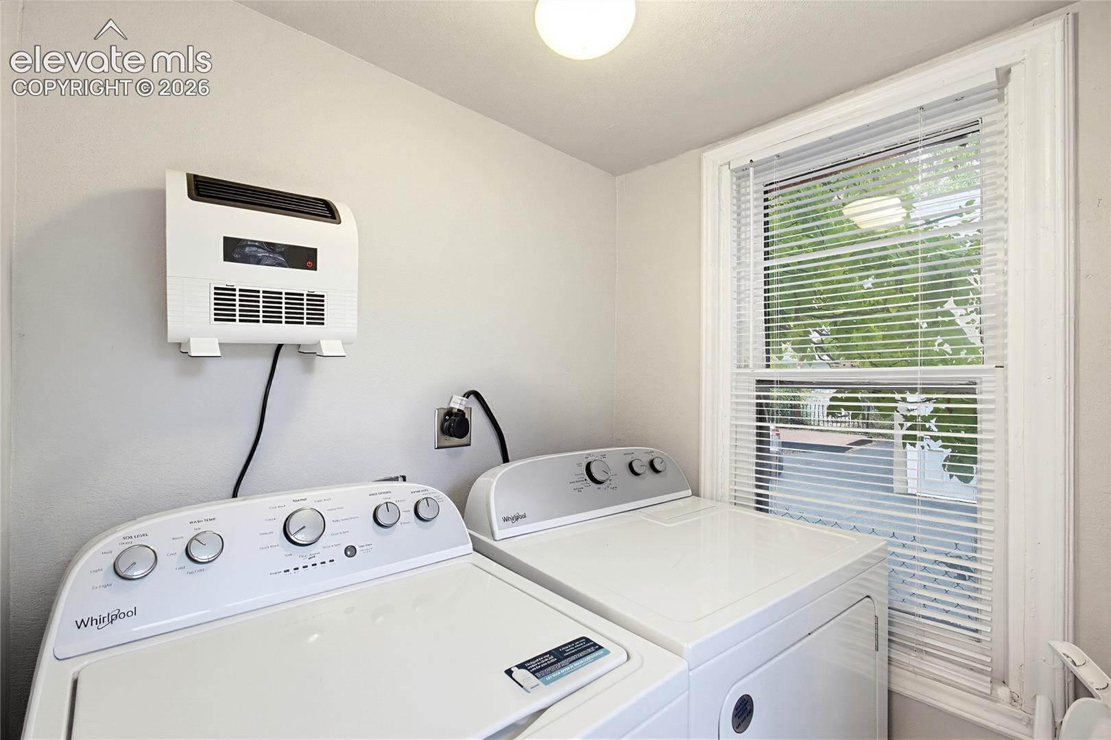 Window with blinds, wall-mounted heater, and ceiling-mounted light fixture