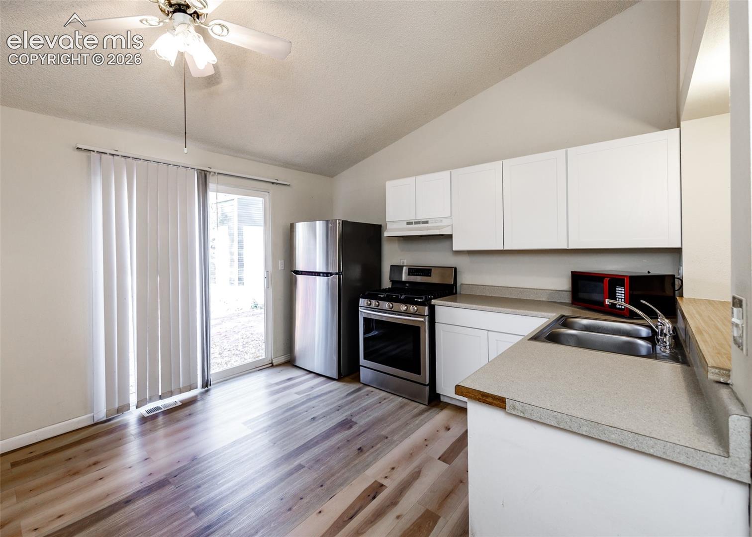 Kitchen featuring wood-finish flooring, white cabinetry, stainless steel appliances, neutral countertops, and sliding glass door