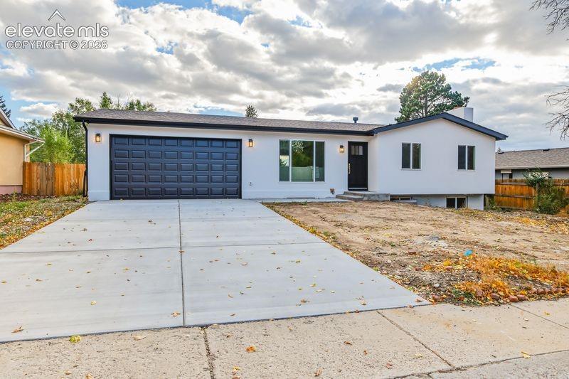 Single-level exterior featuring crisp white siding, an attached two-car garage with a paneled door, a concrete driveway, and black-framed exterior light fixtures