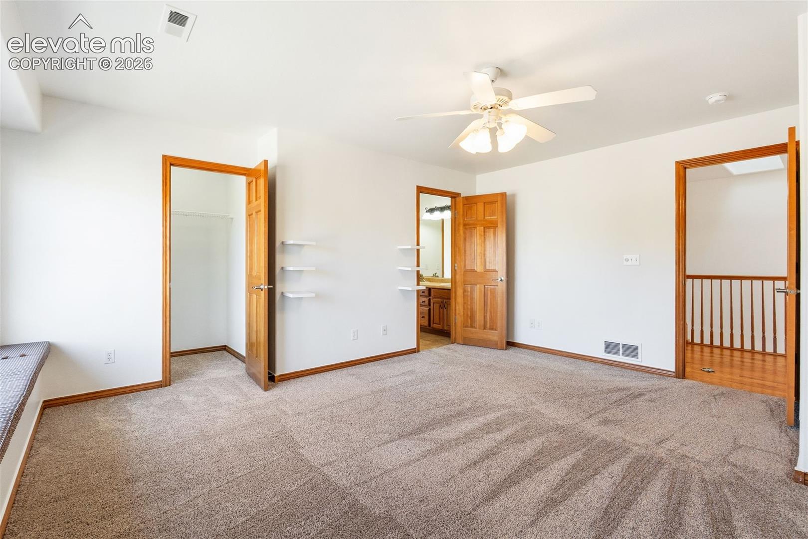 Interior space featuring wall-to-wall carpeting, built-in wall shelving, wood-finish door frames, a multi-blade ceiling fan with integrated lighting, and a wood-slat staircase railing