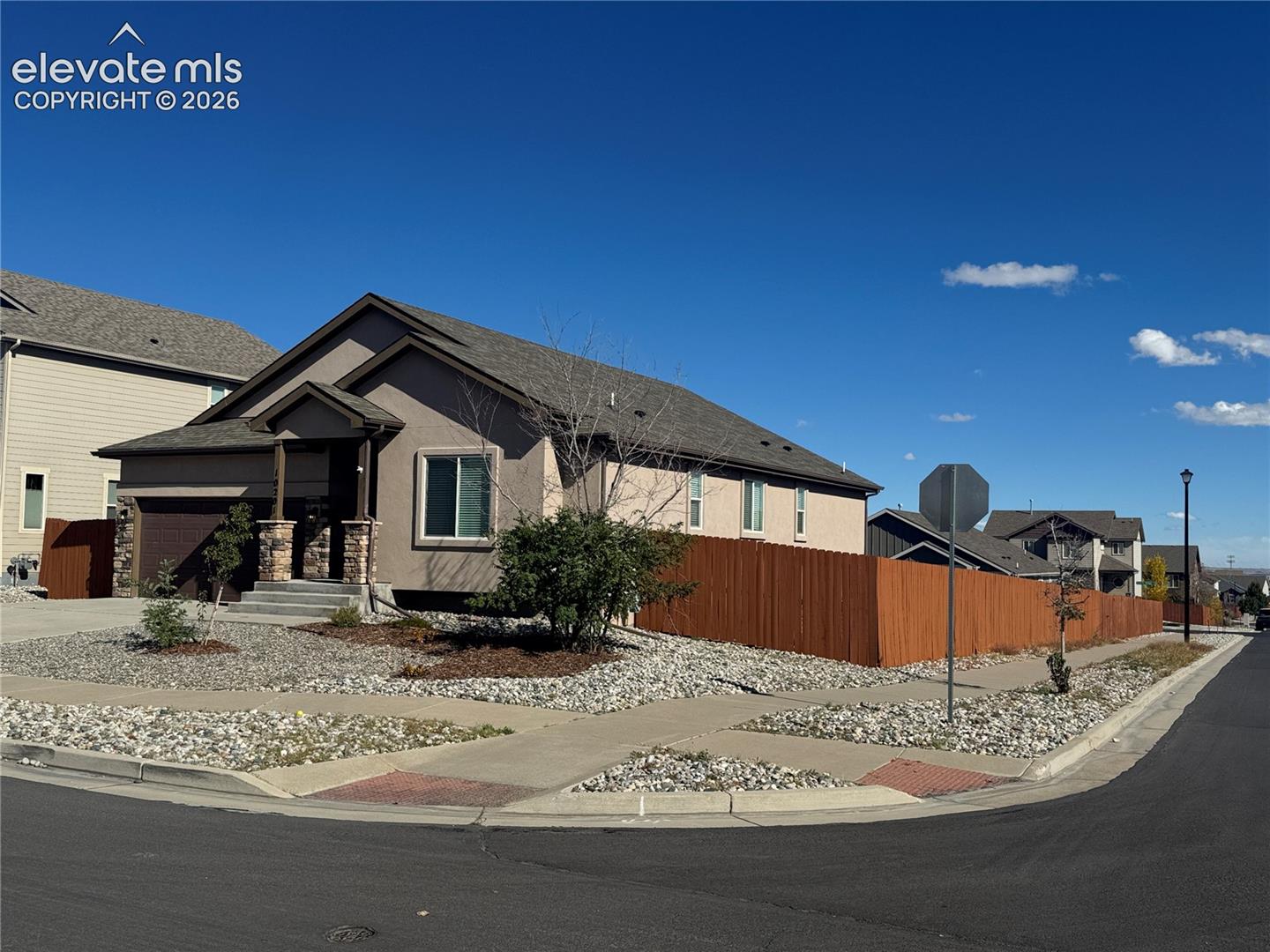 Single-story residence featuring a neutral stucco exterior, covered front entryway with stone column accents, and a fenced side yard with low-maintenance rock landscaping