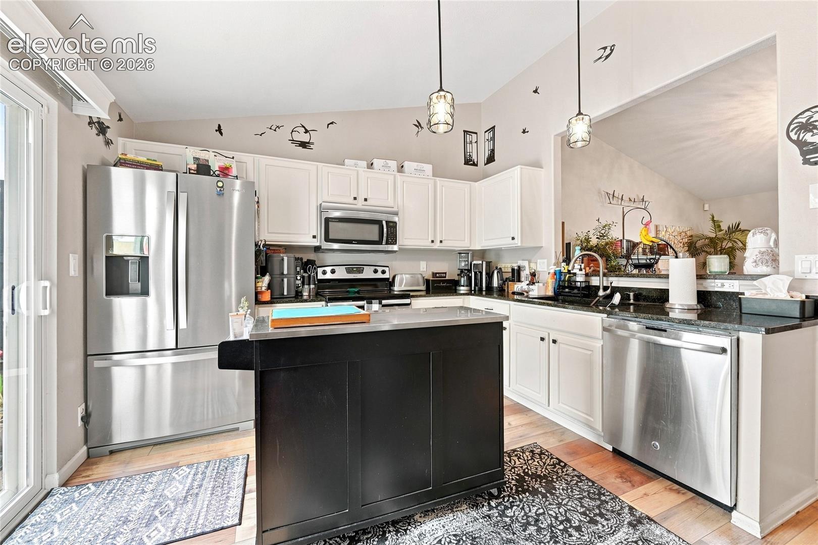 Kitchen featuring white cabinetry, dark stone countertops, stainless steel appliances, a center island with a contrasting black finish, and pendant lighting