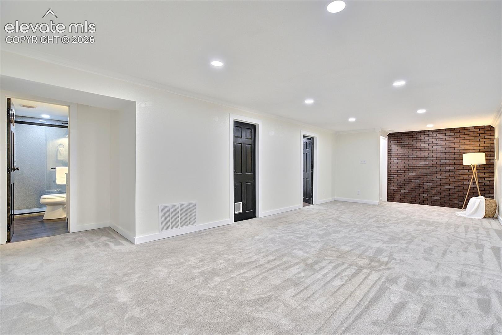 Interior space featuring recessed lighting, a dark brick accent wall, neutral carpeting, and black paneled interior doors