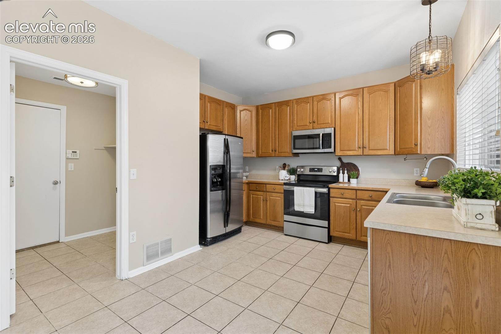 Kitchen featuring wood cabinetry, stainless steel appliances, tile flooring, stone-finish countertops, and an industrial-style pendant light