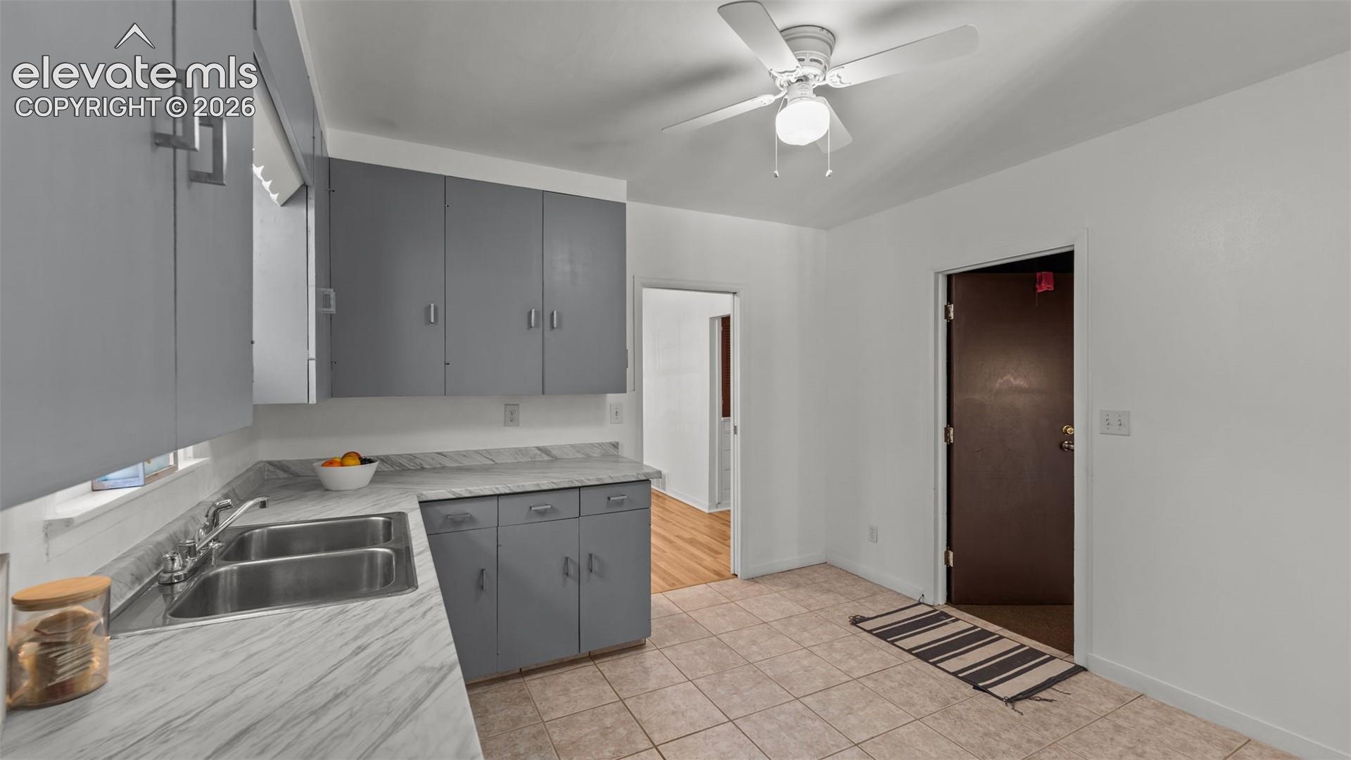 Kitchen featuring gray cabinetry, a dual basin stainless steel sink, wood-finish countertops, and a ceiling fan with integrated lighting