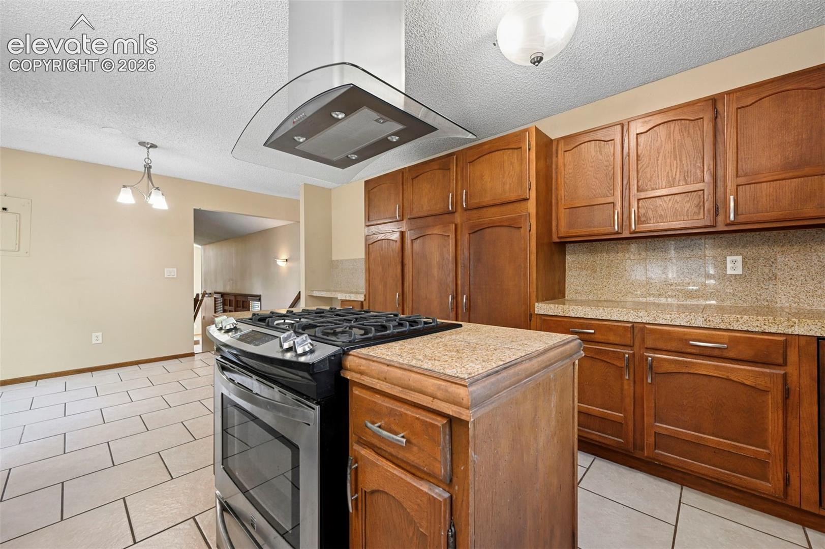 Kitchen featuring wood cabinetry, stone-finish countertops, tile flooring, a stainless steel gas range, and a glass-and-stainless steel range hood