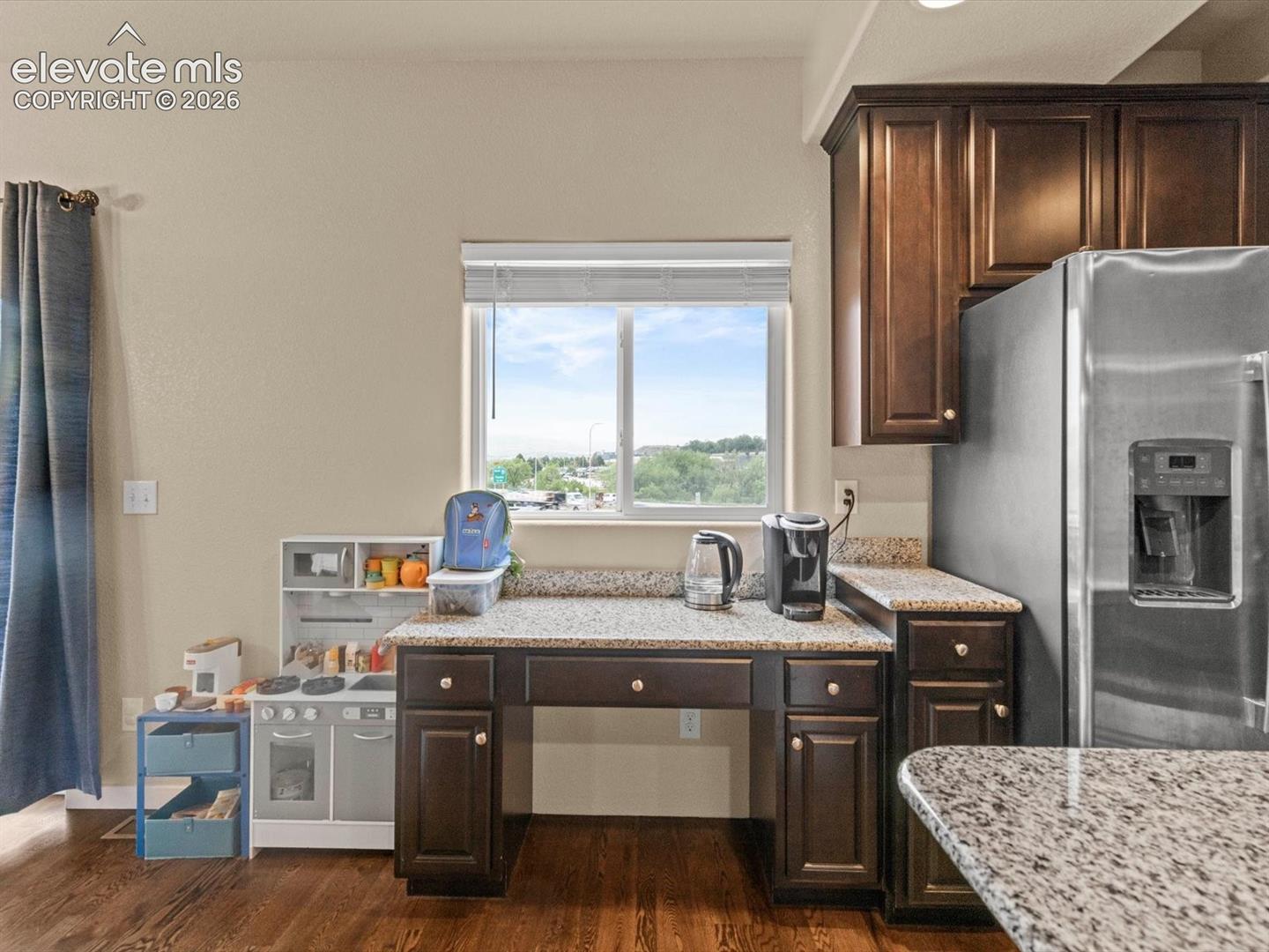 Kitchen featuring dark wood cabinetry, light speckled countertops, stainless steel refrigerator, and wood-finish flooring