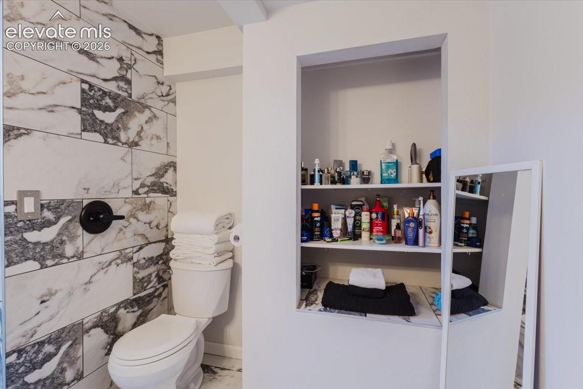 Bathroom featuring large format marble-look tile, a wall-mounted shower control with matte black finish, and a built-in shelving unit with three levels