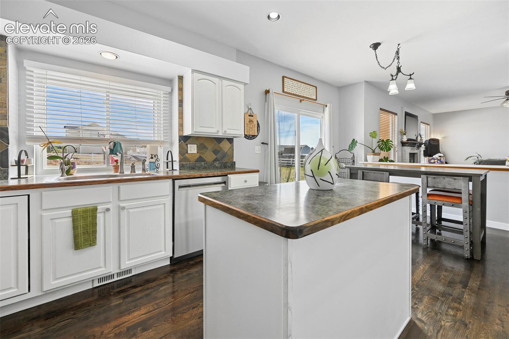 Kitchen featuring white cabinetry, dark wood-finish flooring, a central island with a dark countertop, and a tiled backsplash
