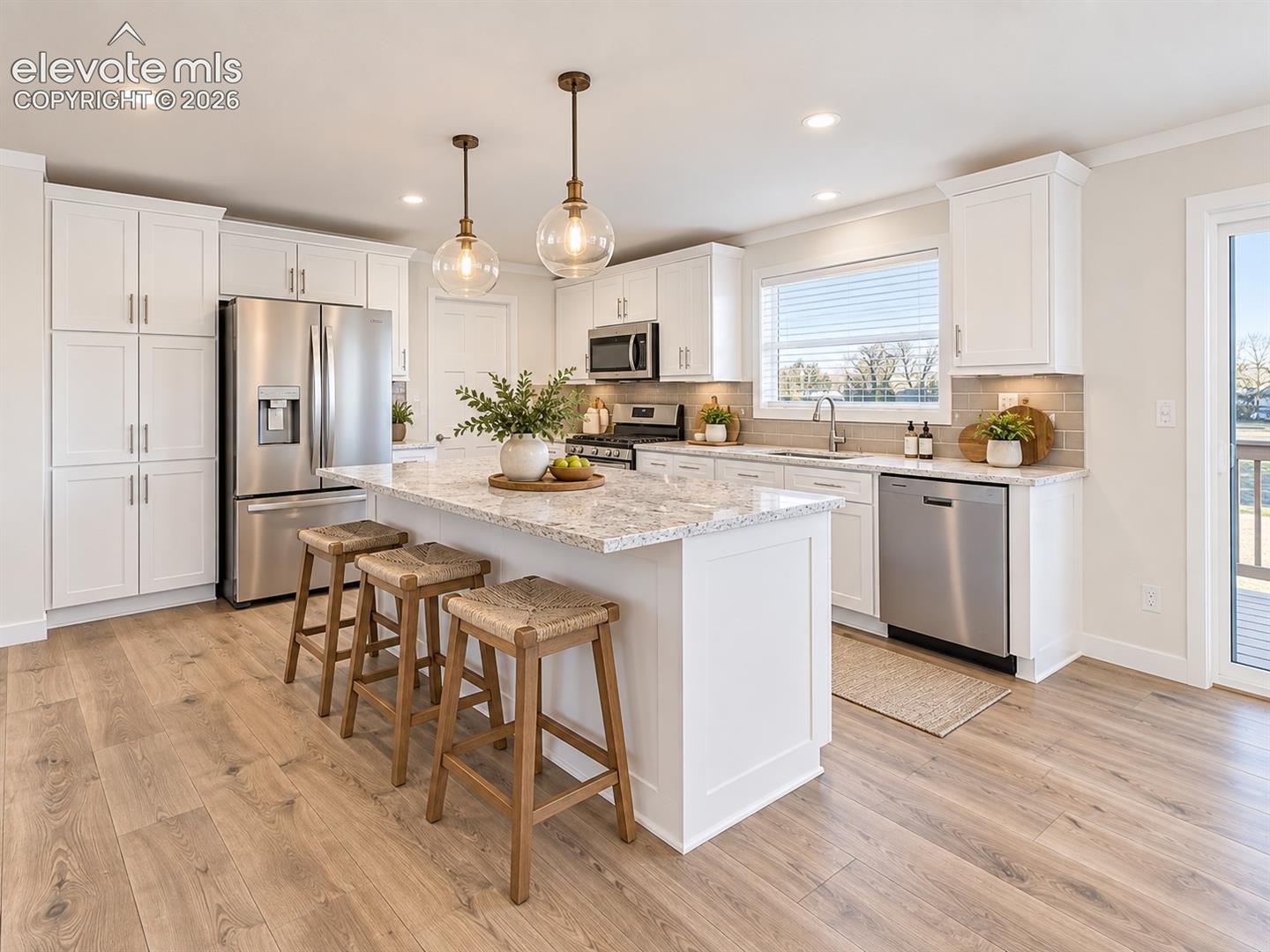 Another view highlights the generous island, abundant cabinetry, stainless steel appliance package, pendant lighting, and window above the sink for added natural light.