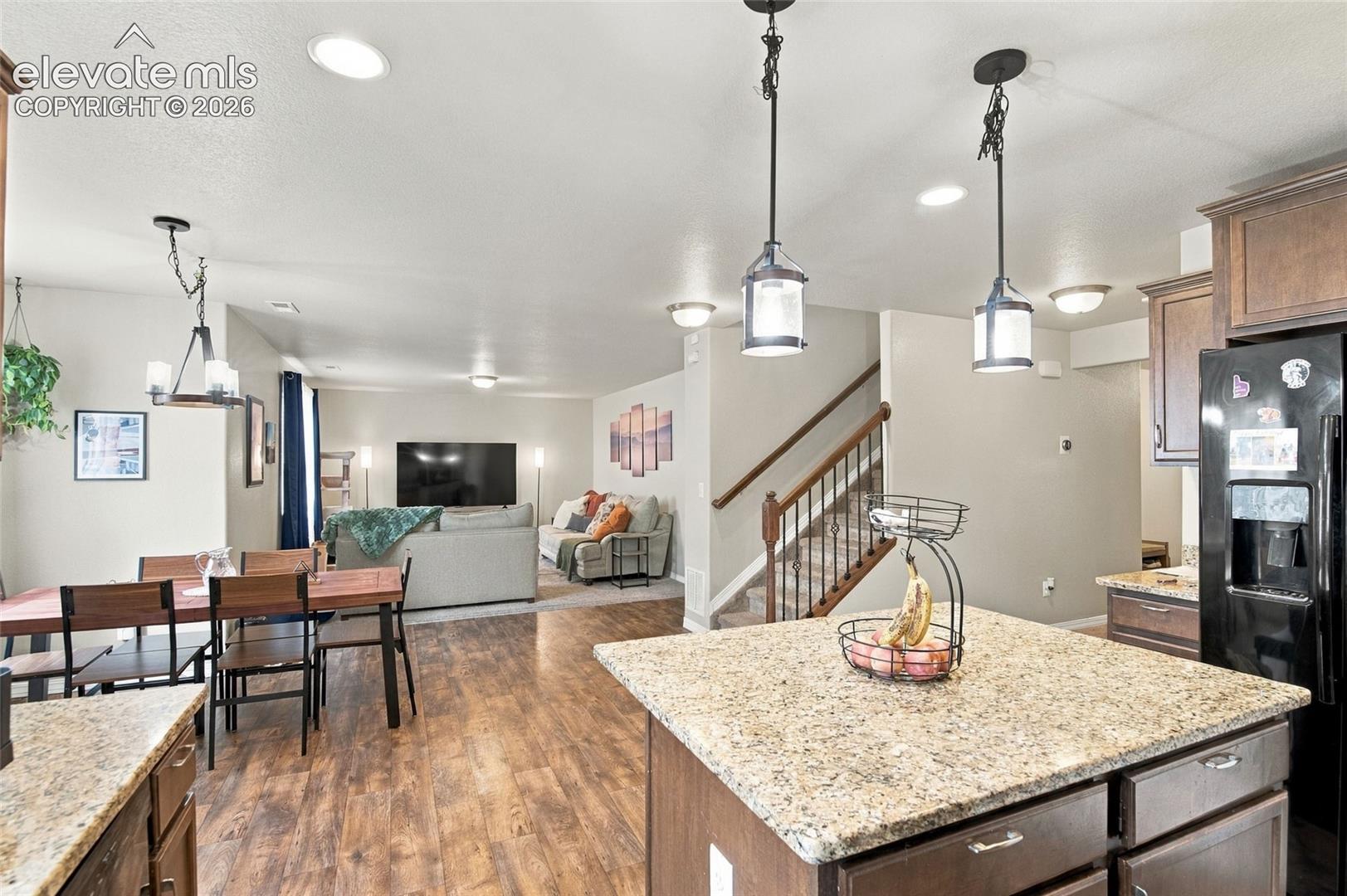 Kitchen featuring a central island with a stone-finish countertop, dark-toned cabinetry, recessed lighting, wood-finish flooring, and pendant lighting