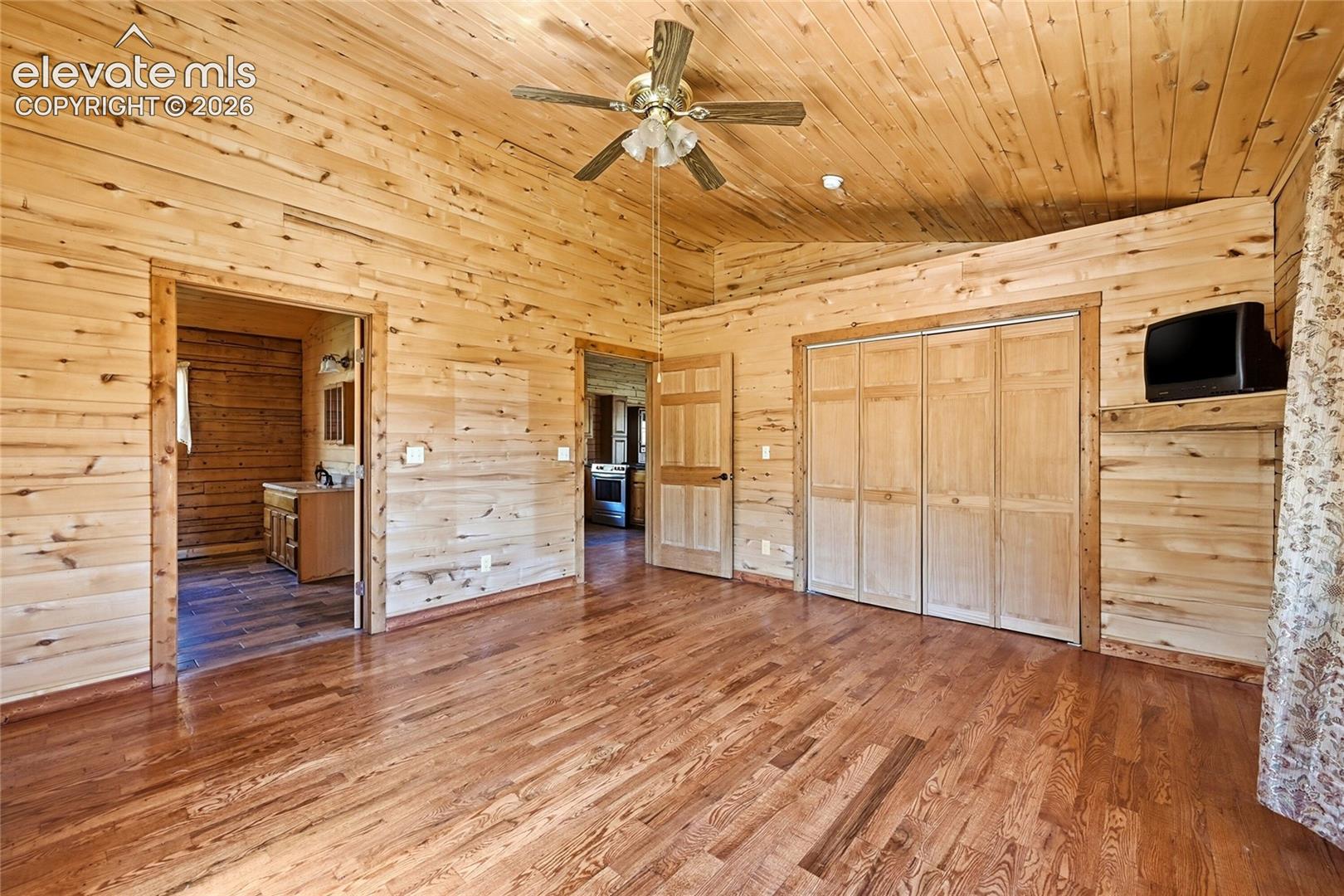 Vaulted wood-paneled ceilings, wood-paneled walls, wood-finish flooring, bi-fold closet doors, and a ceiling fan with integrated lighting