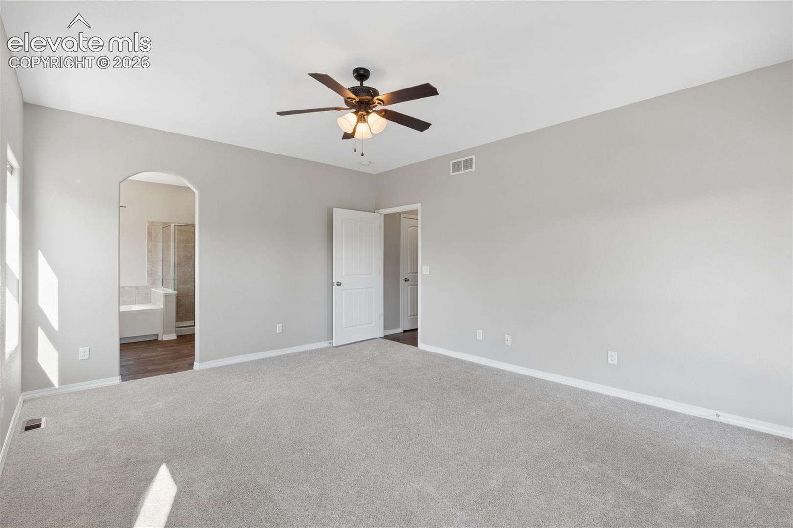 Spacious room featuring light gray wall paint, light gray carpet, and a dark-toned ceiling fan with integrated lighting