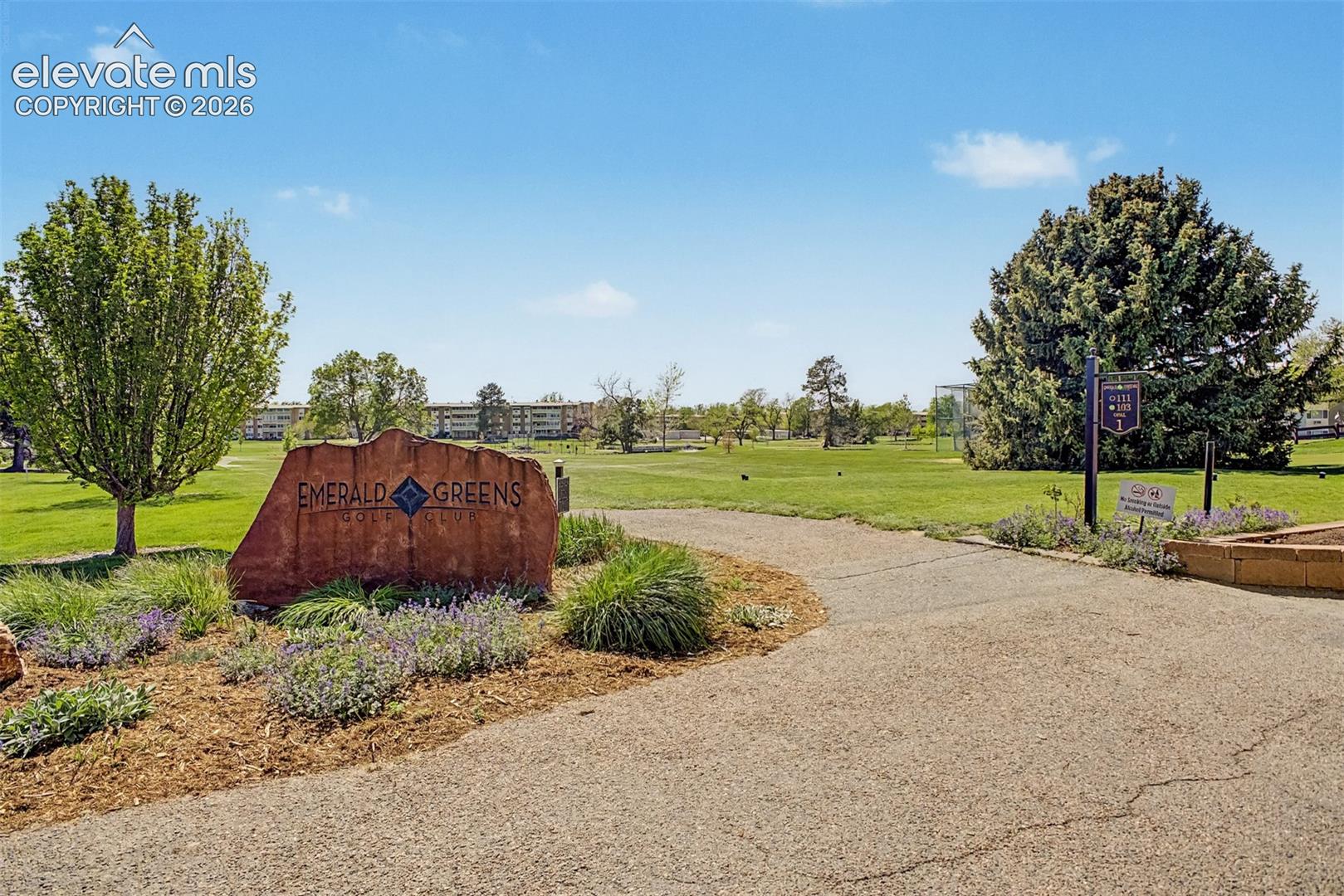 Emerald Greens Golf Club entrance with a stone monument sign, surrounded by landscaped plantings and a paved pathway