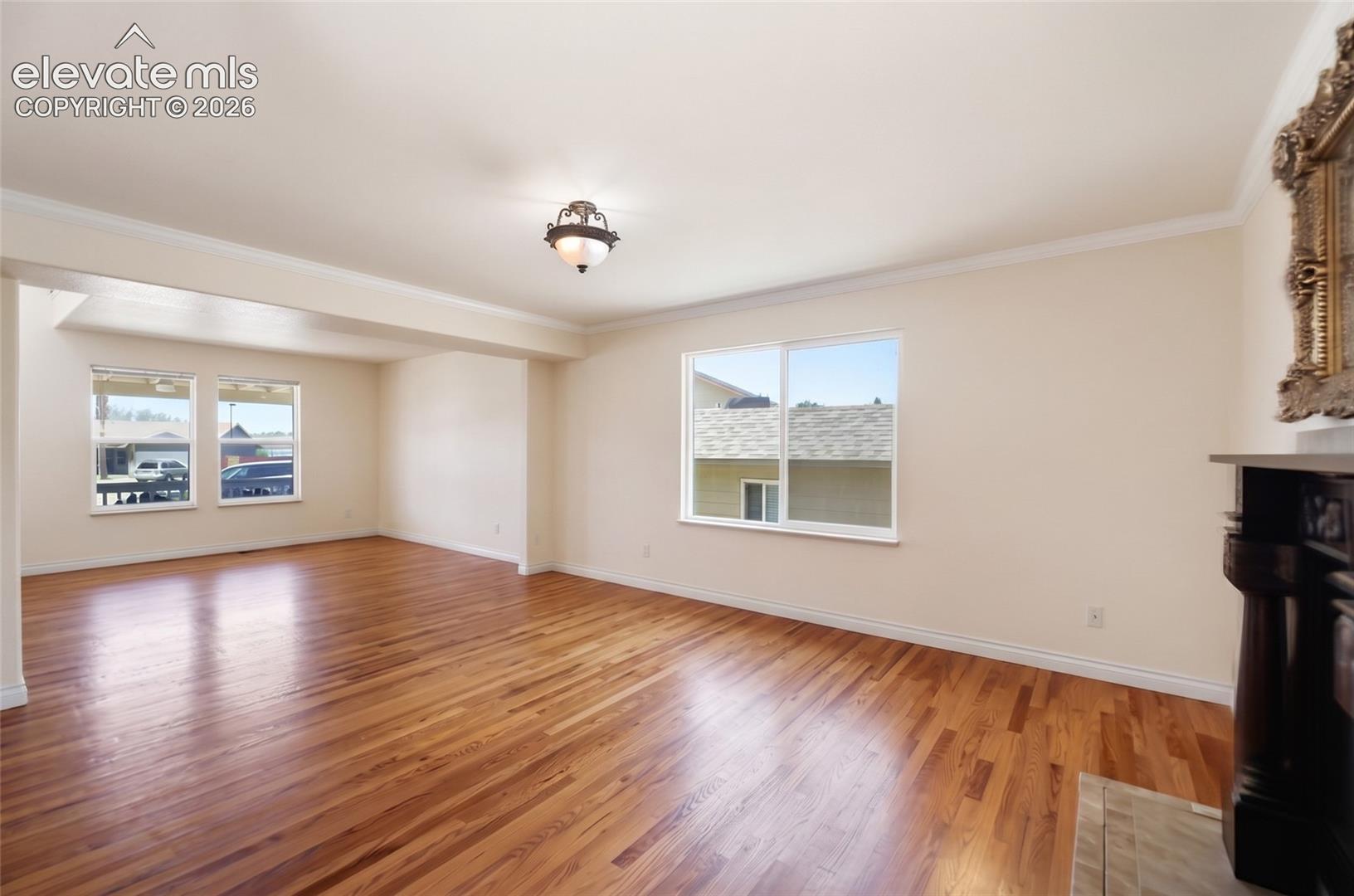 Open concept living space featuring wood-finish flooring, white baseboards, and crown molding