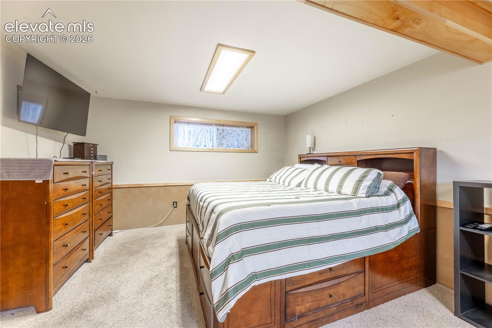 Interior space featuring neutral wall tones, carpeted flooring, a rectangular flush-mount ceiling light, and a horizontal window with natural wood trim