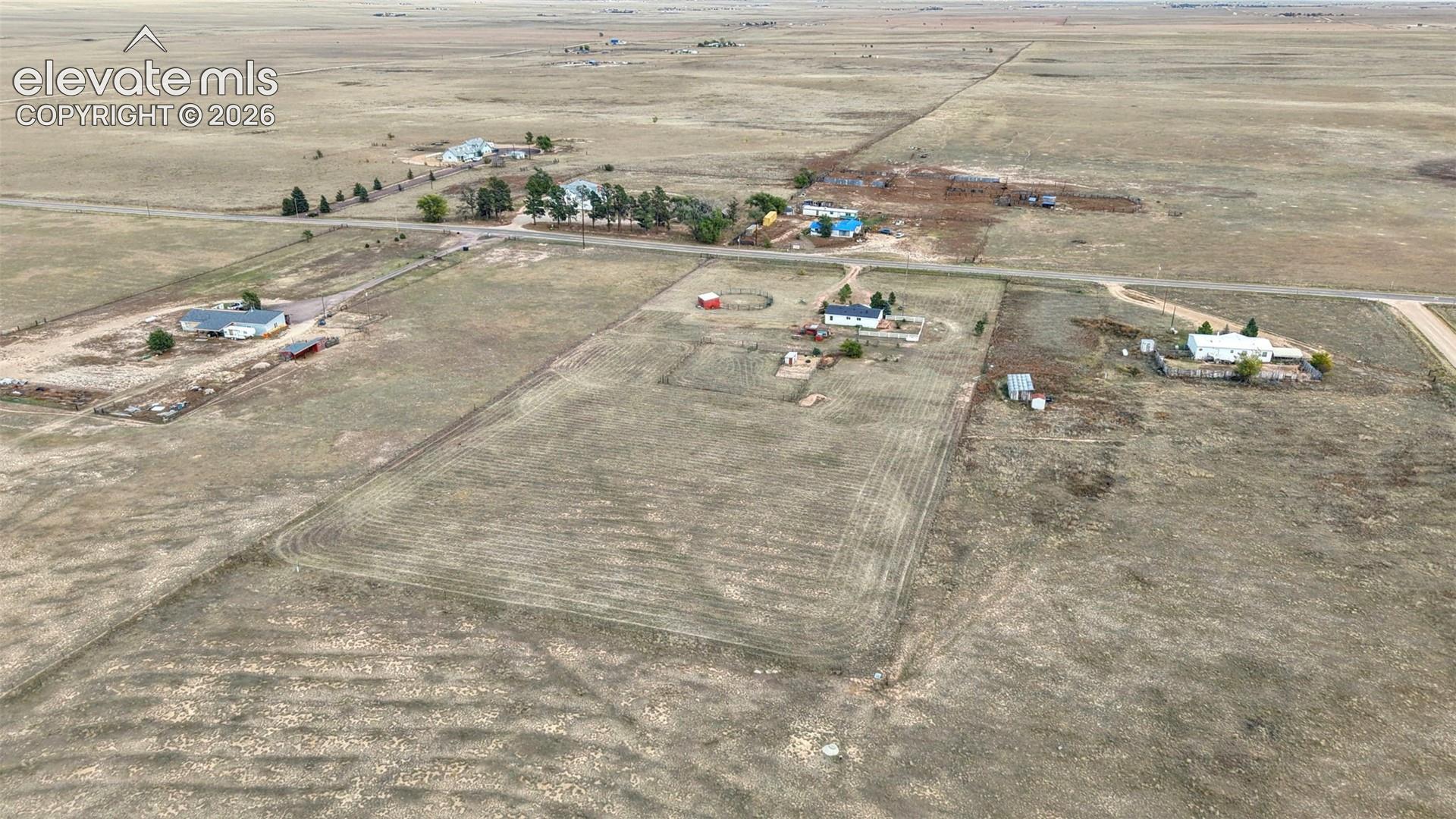 Aerial perspective of a sprawling property featuring expansive open land, a multi-structure building layout, established tree lines, and direct access to a paved roadway