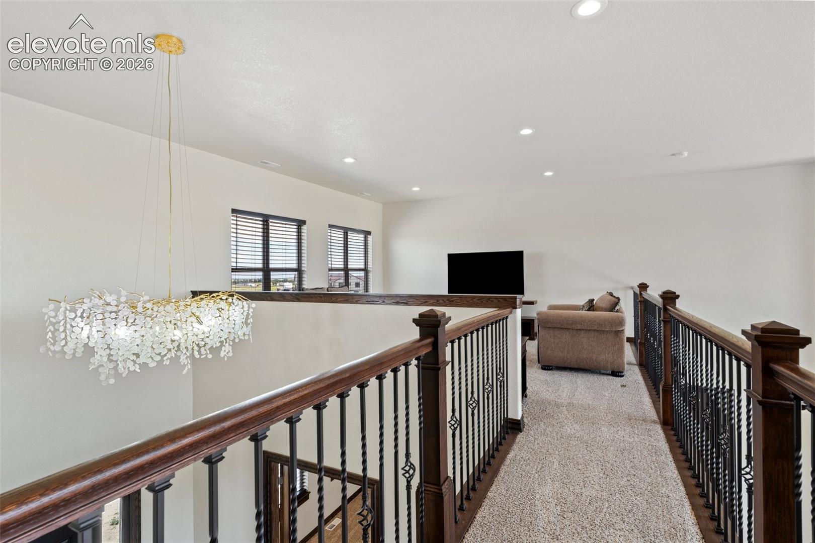 Upper-level hallway featuring a decorative chandelier, dark wood railings with wrought iron spindles, and recessed lighting