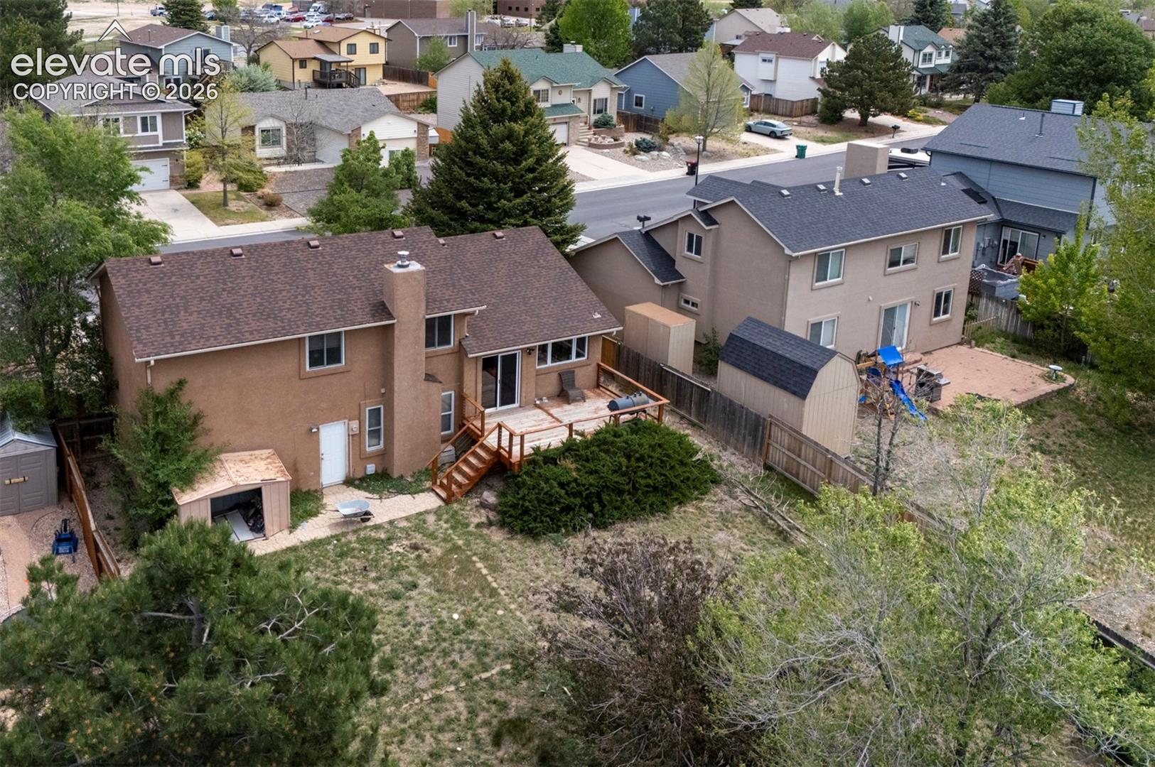 Rear elevation featuring a spacious wooden deck with stairs to the yard, two exterior storage sheds, and mature landscaping