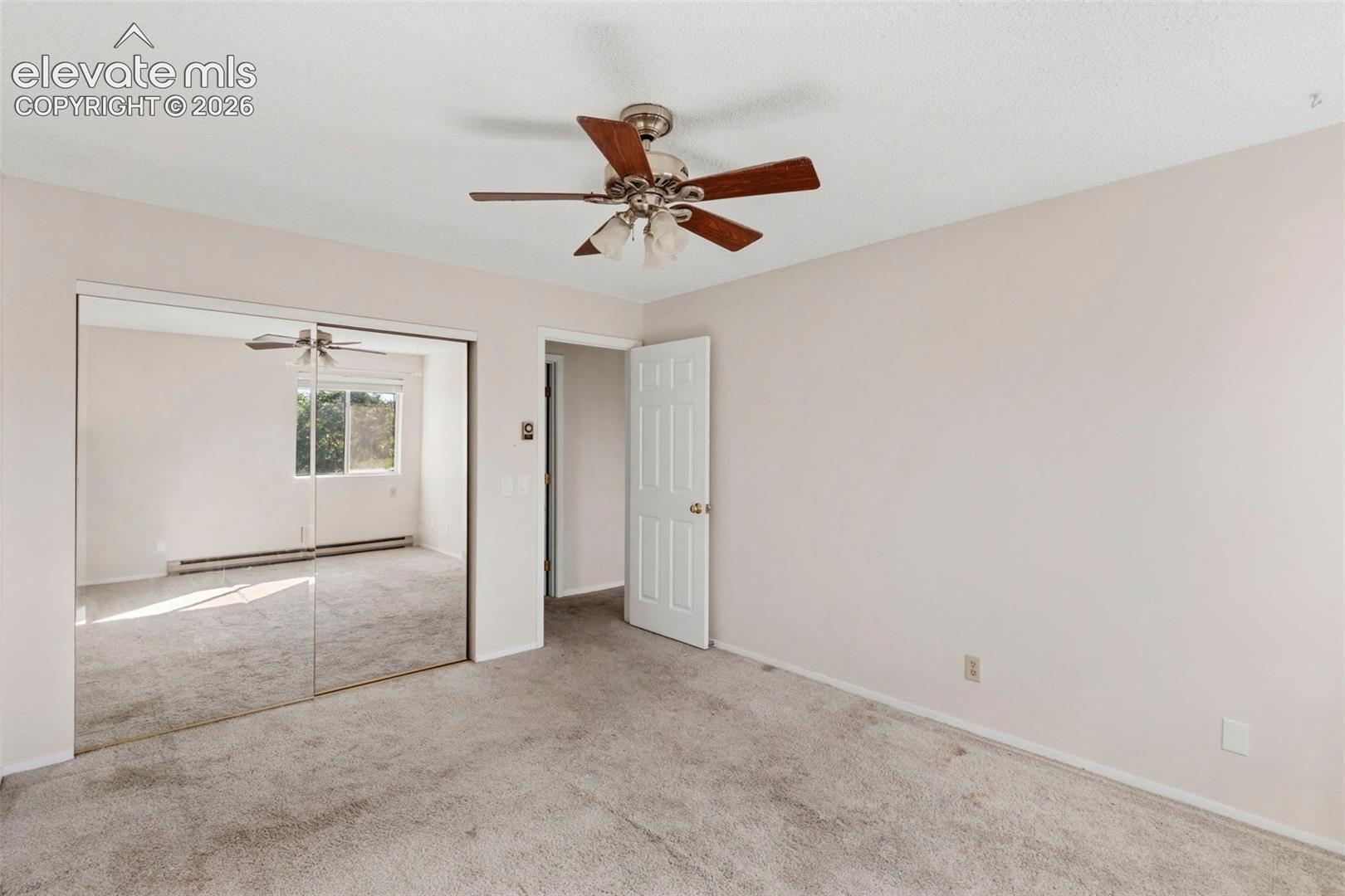 Wall-to-wall carpeting with mirrored closet doors and a ceiling fan