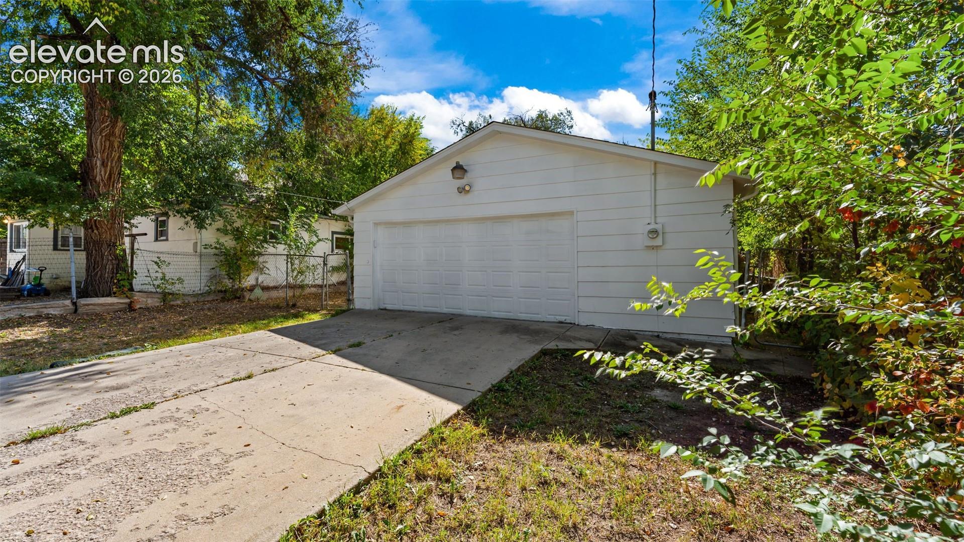 Spacious two-car garage with white paneled overhead door and concrete driveway, framed by mature trees and established landscaping