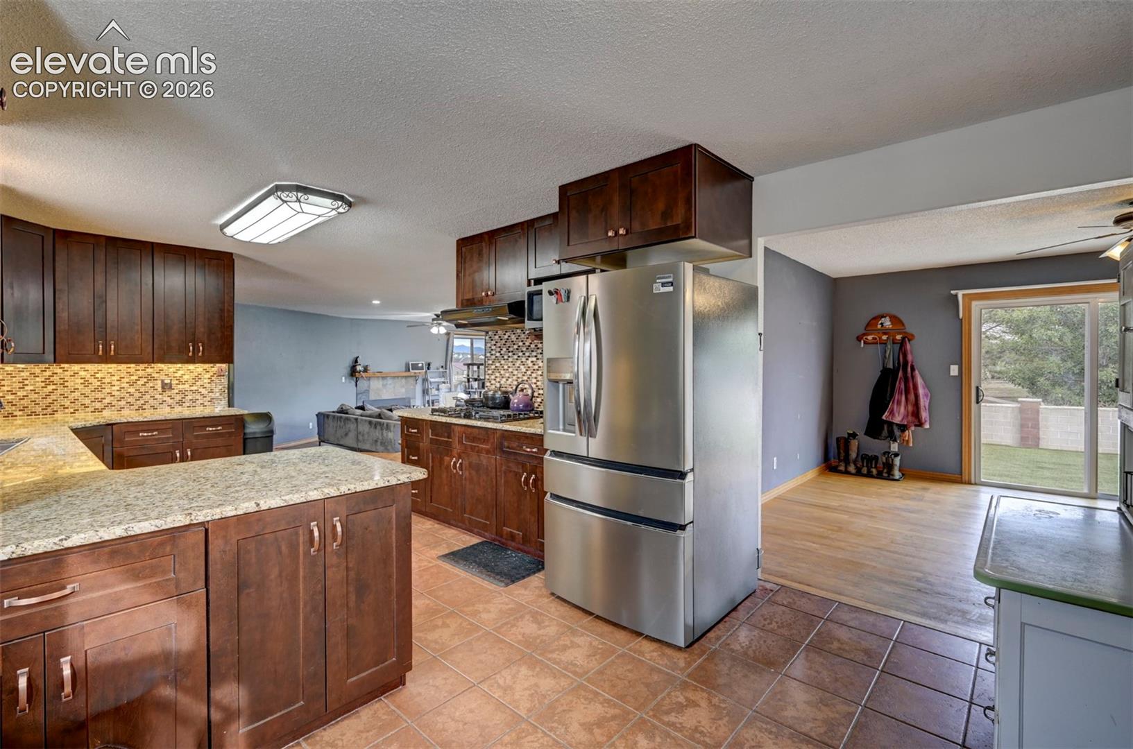Kitchen featuring stainless steel appliances, wood-finish cabinetry, stone countertops, and a mosaic tile backsplash