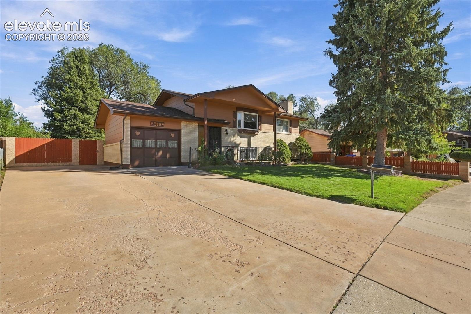 Multi-level exterior featuring brick and siding facade, bay window, attached garage, expansive concrete driveway, and perimeter fencing