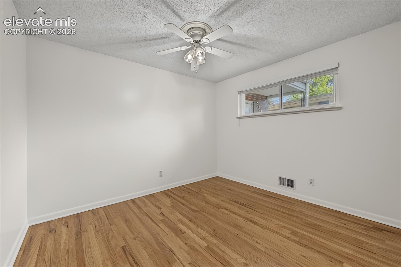 Room featuring wood-finish flooring, a textured ceiling, and an integrated ceiling fan with a light fixture