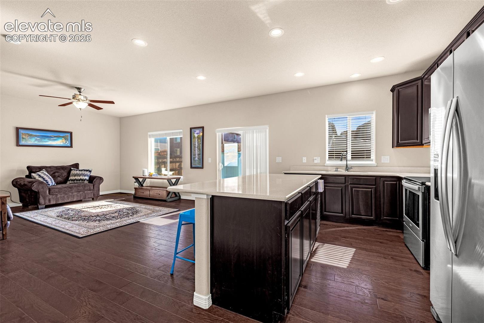 Open-concept living space featuring wood-finish flooring, recessed lighting, a ceiling fan, and a kitchen island with seating