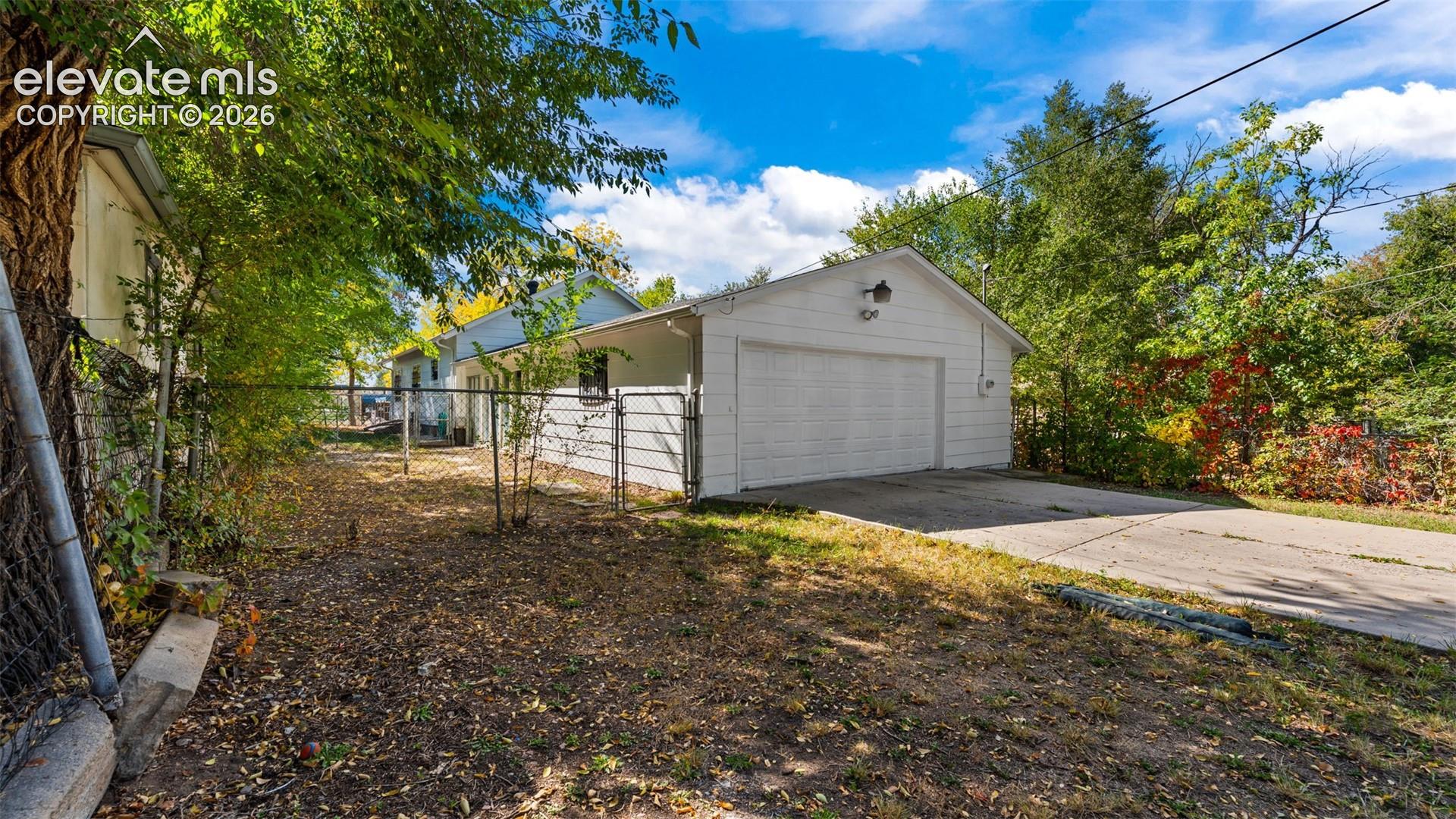 Spacious backyard with mature shade trees and level landscaping, featuring a detached two-car garage with overhead door and concrete driveway approach