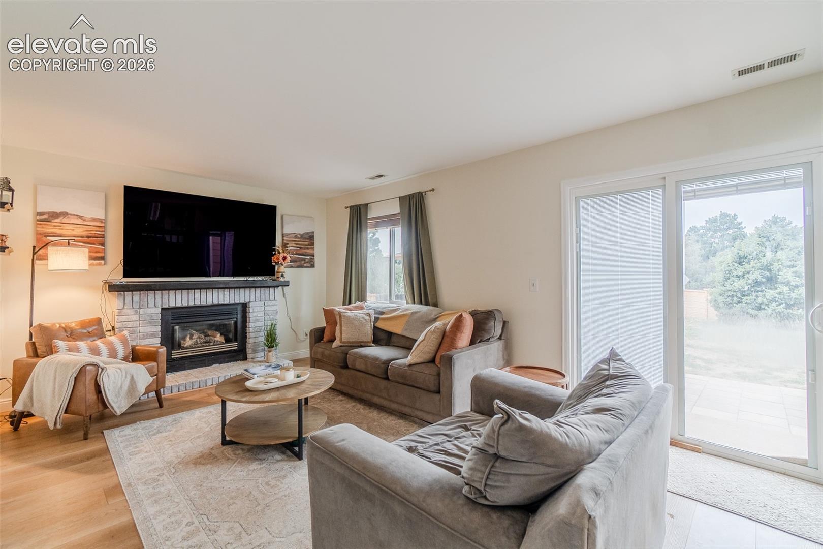 Living area featuring a stone-clad fireplace, wood-finish flooring, and sliding glass door with built in blinds
