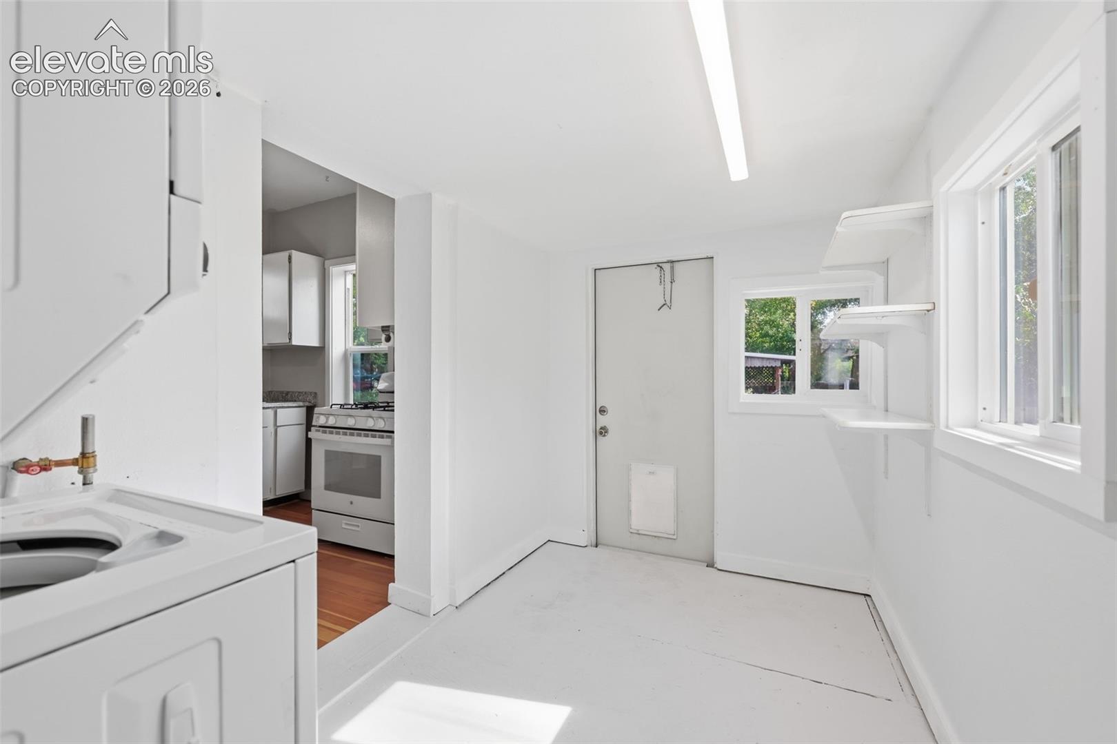 Laundry room featuring an integrated washer and dryer unit, built-in shelving, a single window, and outside door access.