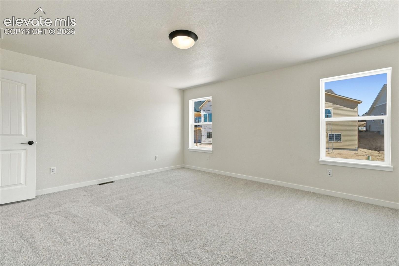 Spacious Primary Bedroom room with soft white walls, light-light gray carpeting, and a flush-mount ceiling light.