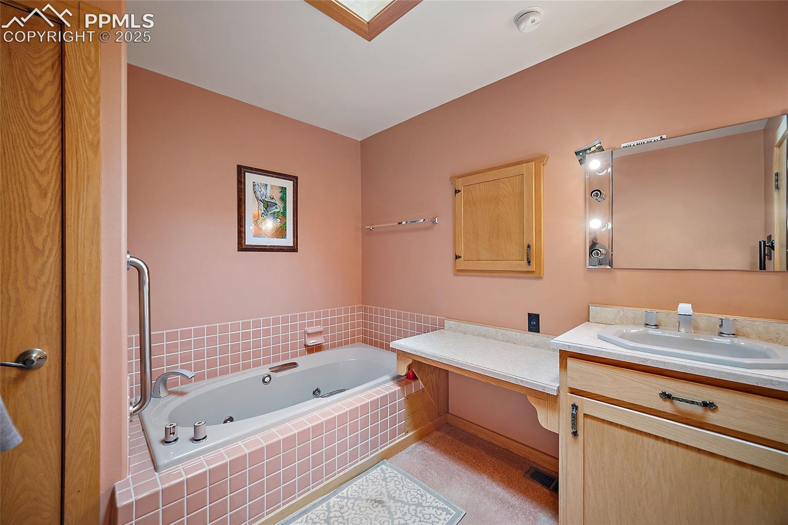 Full bathroom featuring vanity, a whirlpool tub, and a skylight