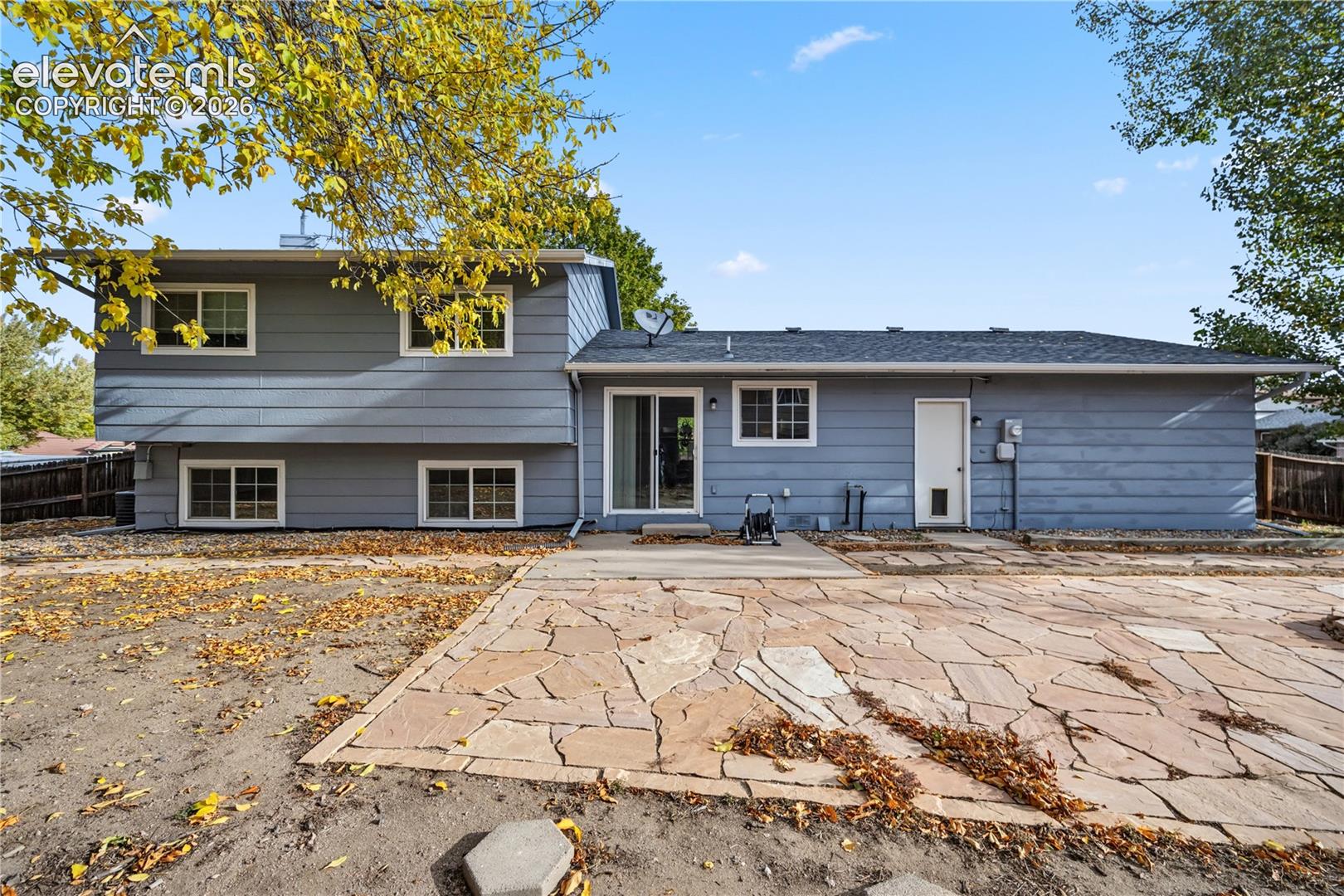 Rear elevation featuring horizontal lap siding, multi-level architectural design, sliding glass patio door, and expansive flagstone hardscaping