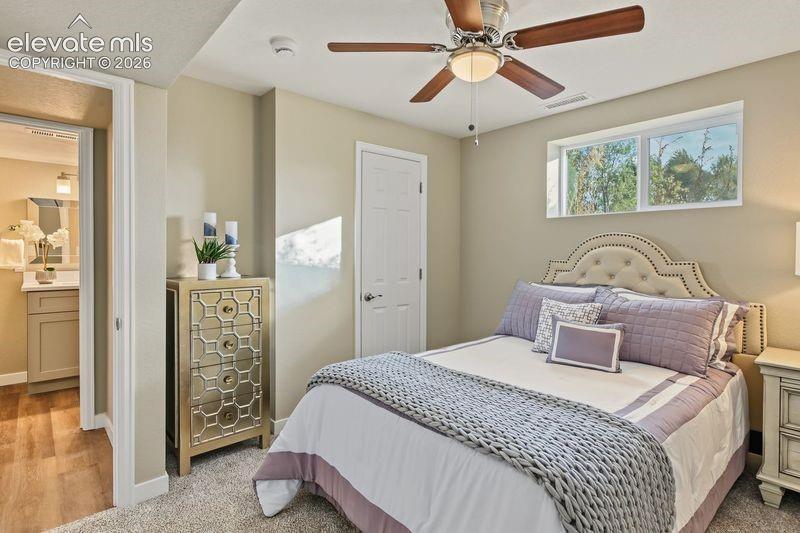 Neutral-toned bedroom featuring wall-to-wall carpeting, a multi-blade ceiling fan with integrated lighting, and a horizontal sliding window