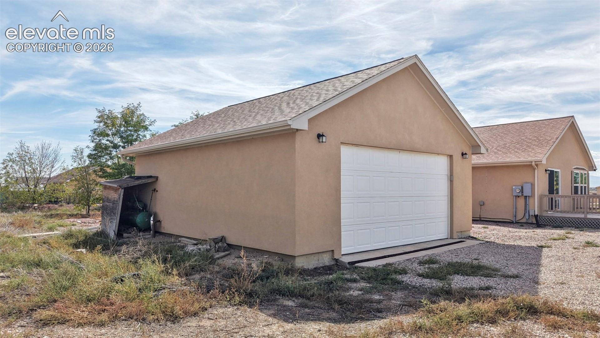 Detached garage structure featuring a stucco exterior, shingled gable roof, and a sectional overhead garage door