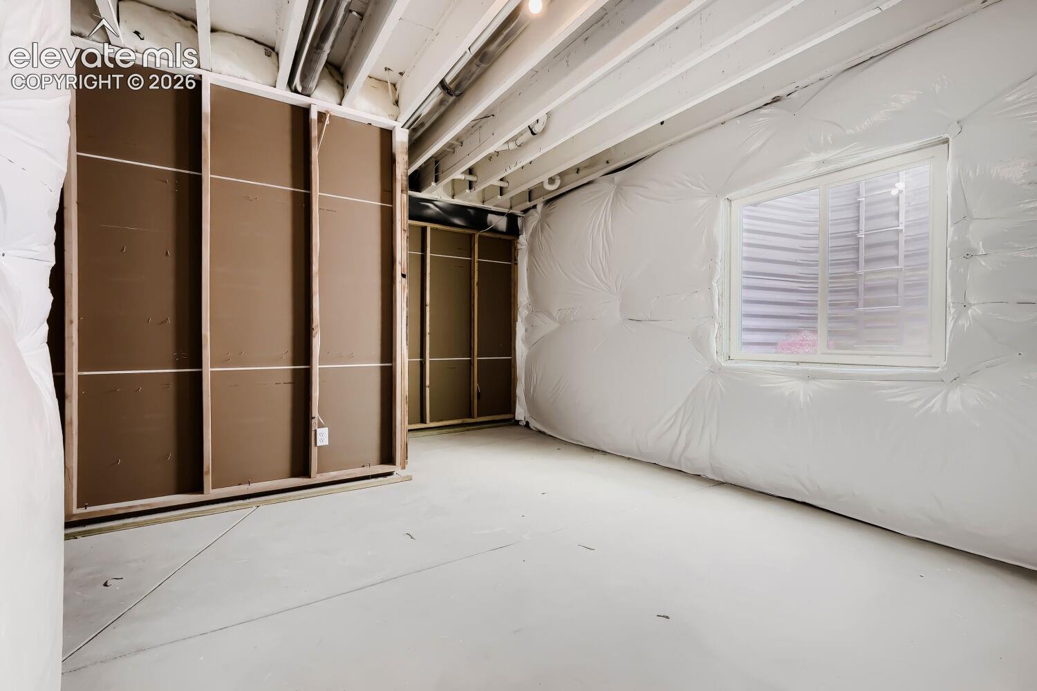 Unfinished basement space featuring a single window and exposed ceiling joists
