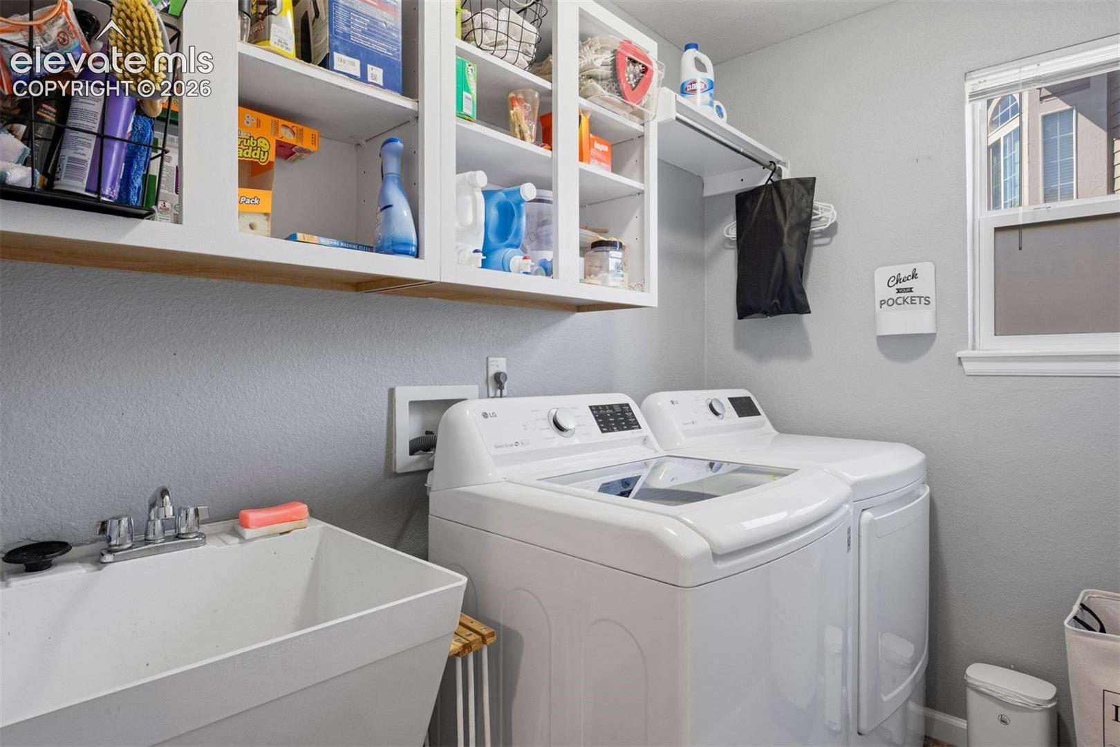 Dedicated laundry area featuring a utility sink with a chrome faucet, overhead white cabinetry, and a window providing natural light